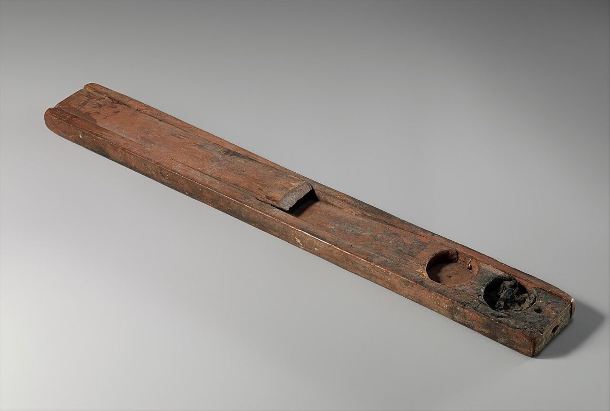 A wooden scribe's palette with wells for black and red ink and a slot for reed pens. Metropolitan Museum of Art, New York.