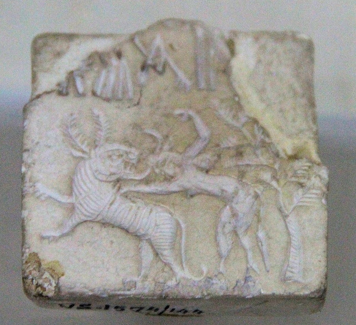 A seal from Harappa with a scene of a figure fighting an animal; above it a partly broken Indus inscription.