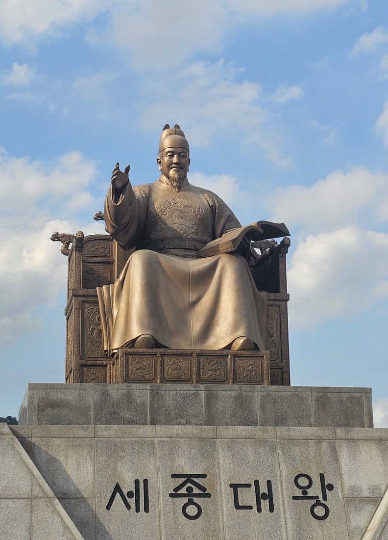 The bronze statue of King Sejong in Gwanghwamun Square, Seoul, unveiled on Hangul Day 2009. The king holds a book; the pedestal reads 세종대왕 Sejong Daewang, “Sejong the Great”.