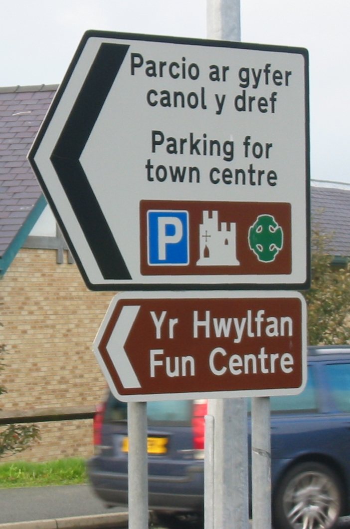 A bilingual direction sign in Caernarfon, north-west Wales, with the Welsh text above the English (Parcio ar gyfer canol y dref – Parking for town centre).