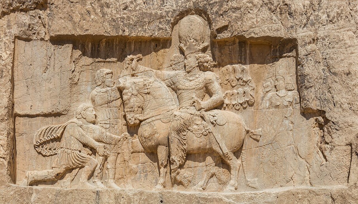 Relief of the triumph of Shapur I over Rome at Naqsh-e Rostam (3rd century CE). A Roman kneels before the king and Shapur holds another by the wrist; they are usually seen as the emperors Philip the Arab and Valerian, but the identification of the figures is disputed.